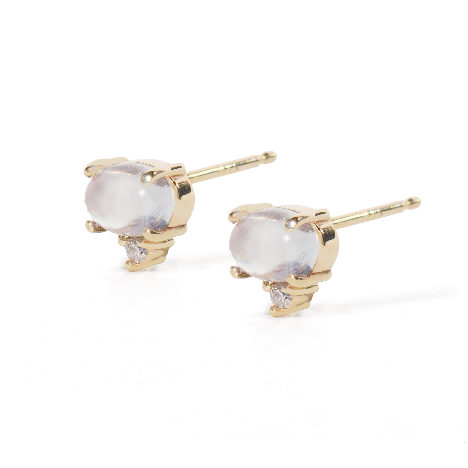 A pair of gold stud earrings featuring oval milky white moonstone cabochons and small clear accent stones, set in polished yellow gold prong settings on a white background.