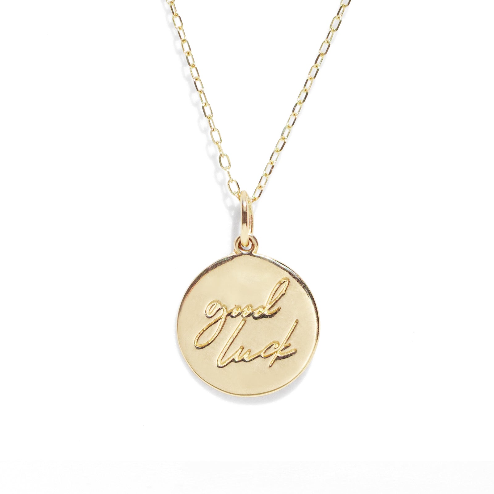 Gold necklace with a round pendant engraved with 'good luck' on a white background
