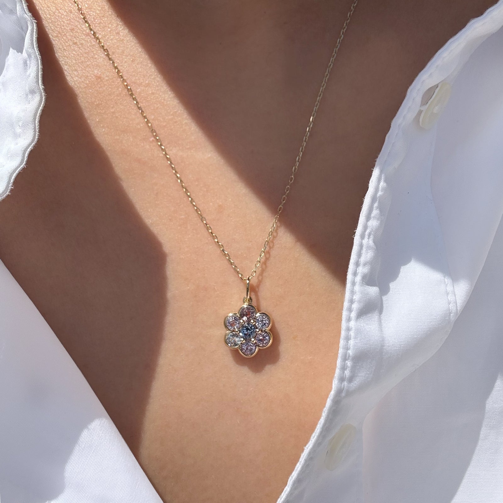 A gold flower-shaped pendant necklace with clear stones, worn on a model's neck over a white collared shirt.