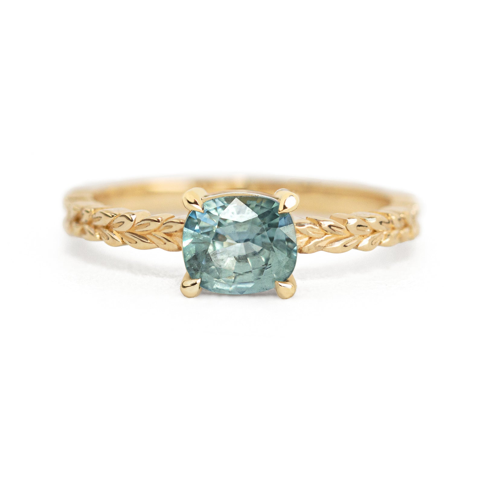 Jamie Park Jewelry -Meadow 1.16ct Cushion Montana Sapphire Ring Indulge in the beauty of nature with our Meadow Montana Sapphire Ring. Featuring a 1.16ct cushion cut sapphire, east-west set on an olive leaf band, this piece is perfect for an engagement ring or a special gift. The Montana sapphire's blue and green hues make it a truly one-of-a-kind piece to celebrate life's special moments.