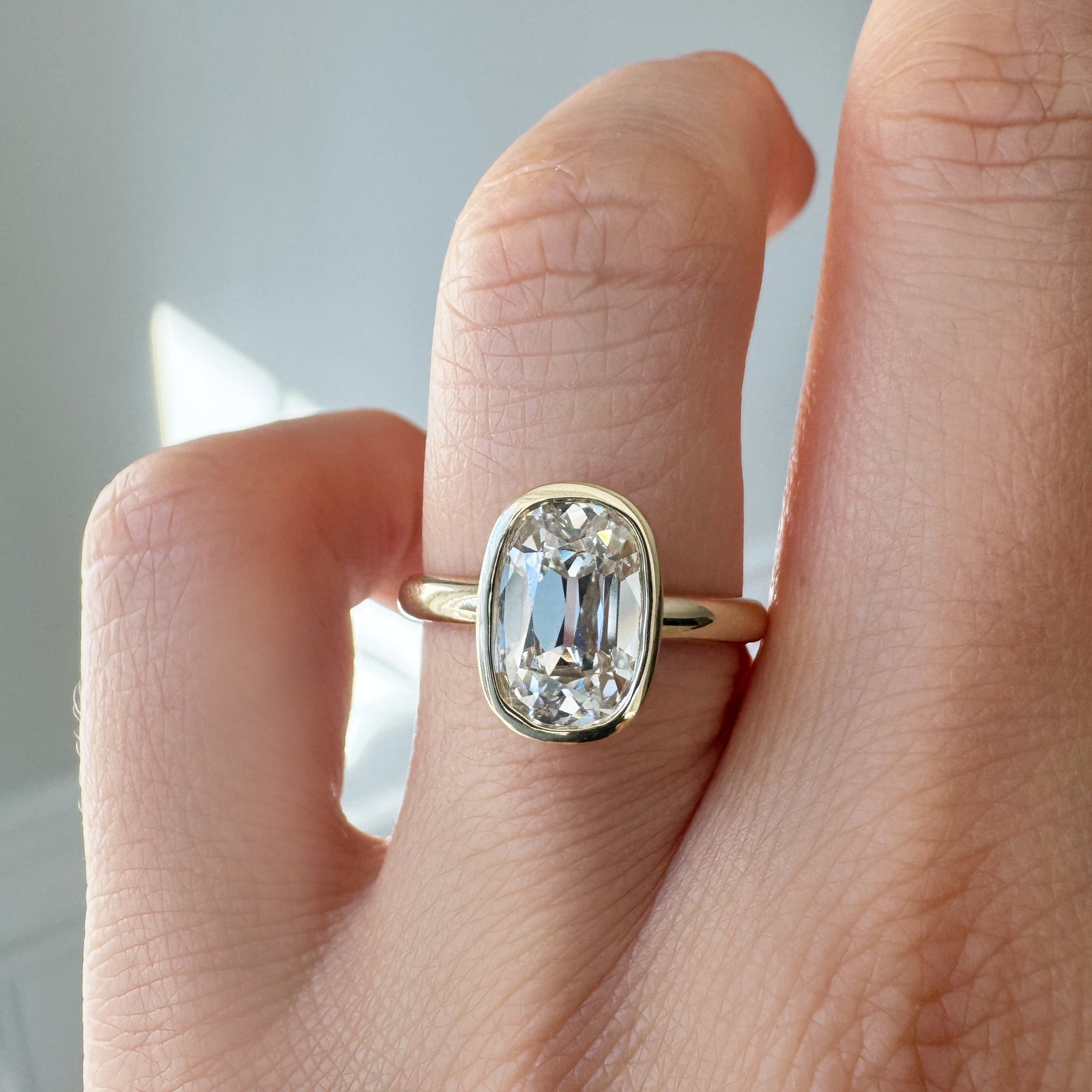 Gold ring with a large diamond on a finger against a neutral background
