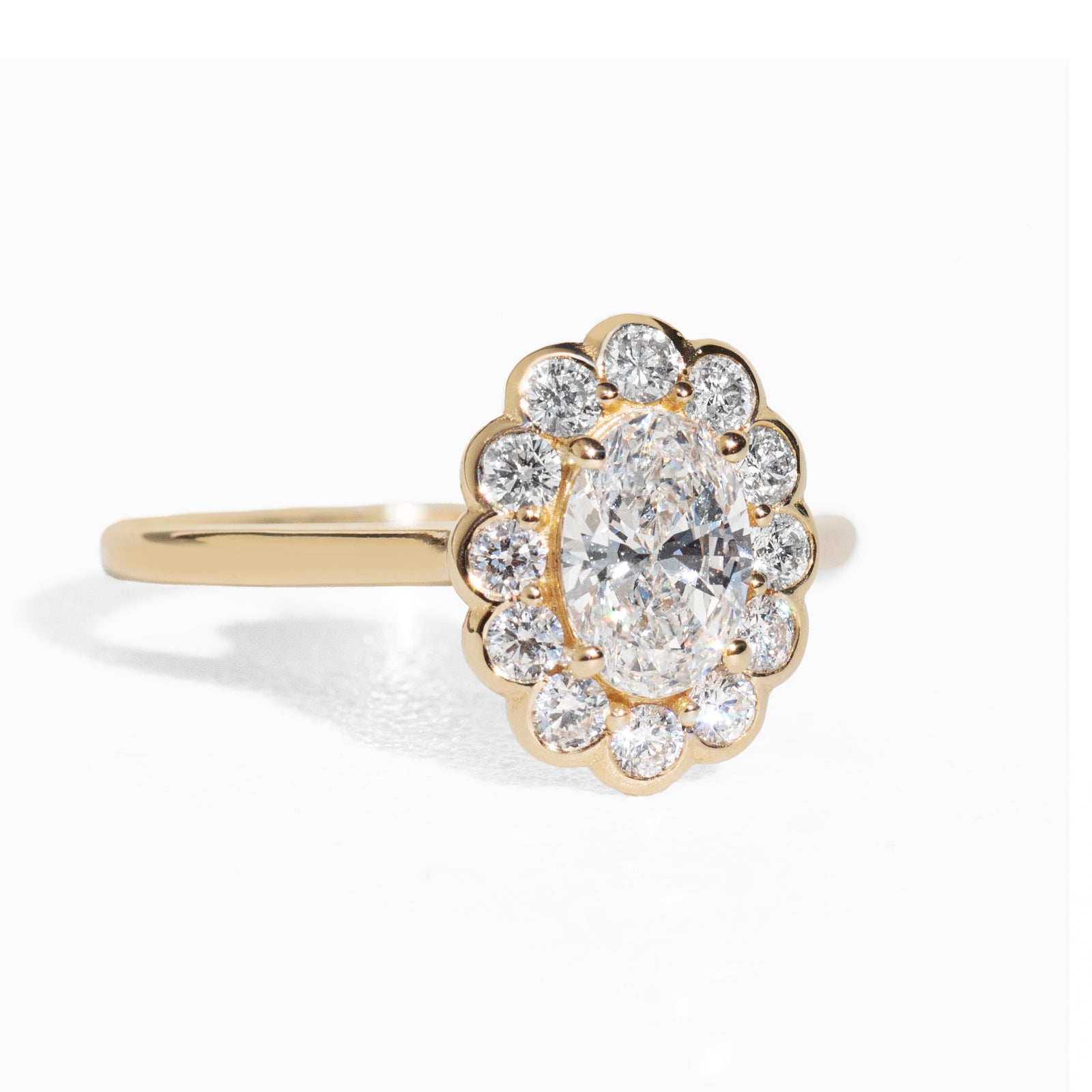 Gold ring with an oval diamond with a halo on a white background