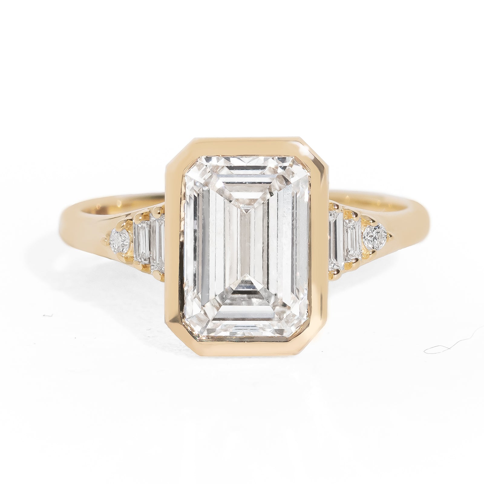 Gold ring with emerald-cut diamond and baguette diamonds on a white background