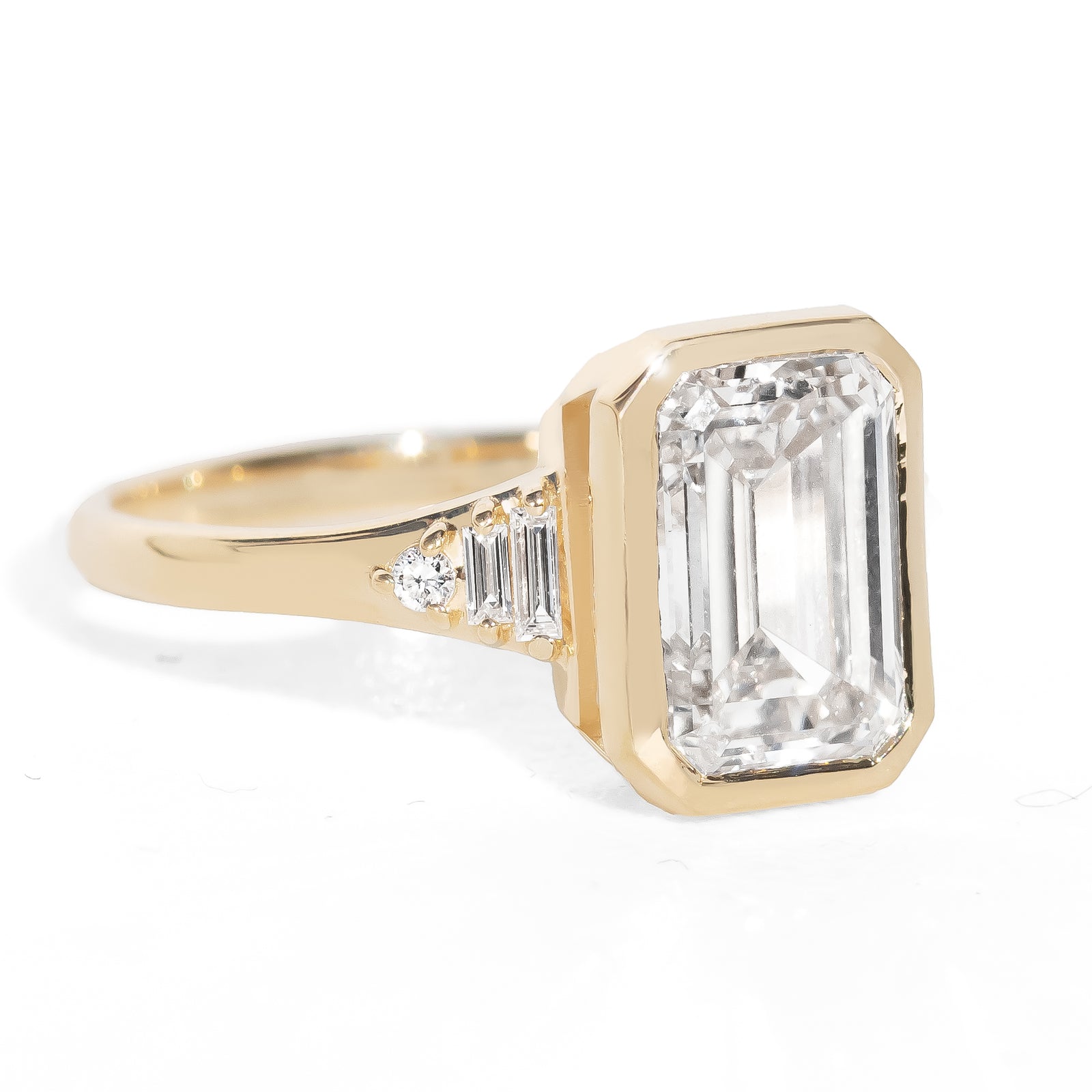 Gold ring with a large emerald-cut diamond and smaller side stones on a white background