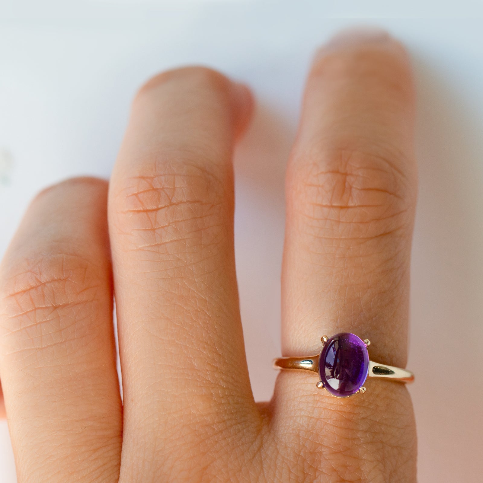 Gold ring with a purple gemstone on a person's finger against a white background