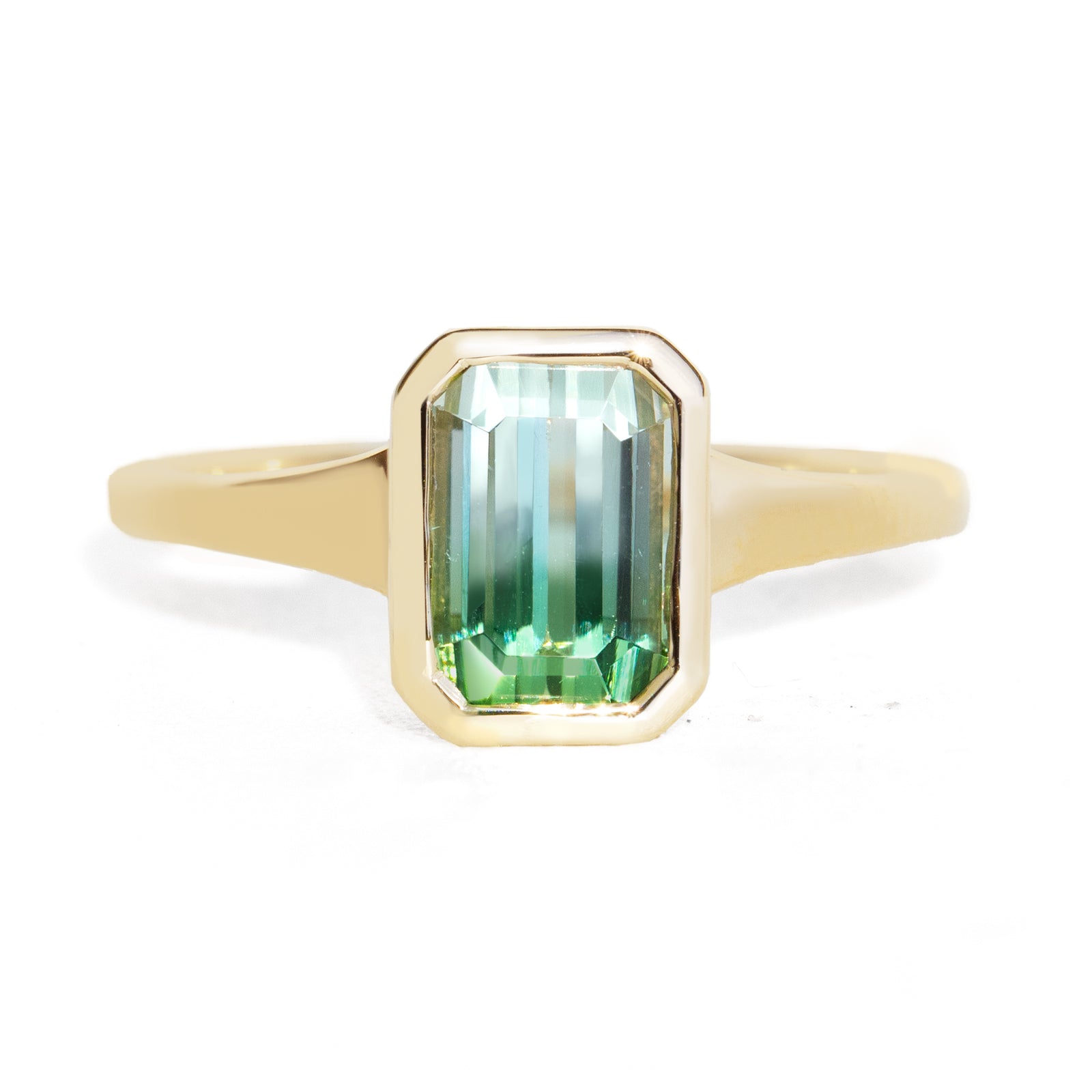 A yellow gold ring featuring a rectangular emerald-cut green gemstone with a gradient of light and dark green, set against a clean white background.