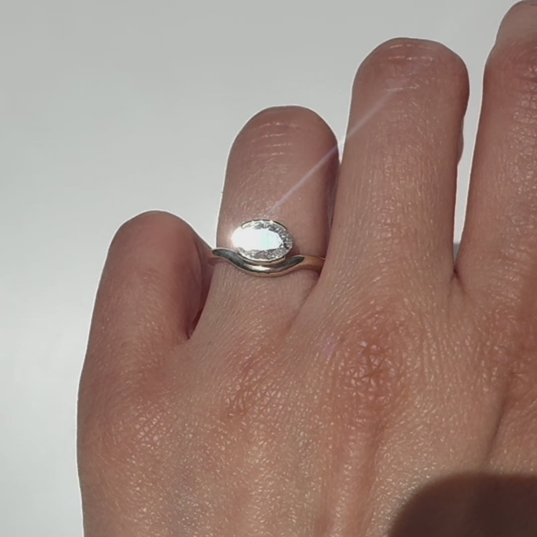 The Flow Ring features a 1 carat oval diamond or moissanite in a half bezel setting. The east west design adds a unique touch to this minimalistic design, making it the perfect subtle statement ring.