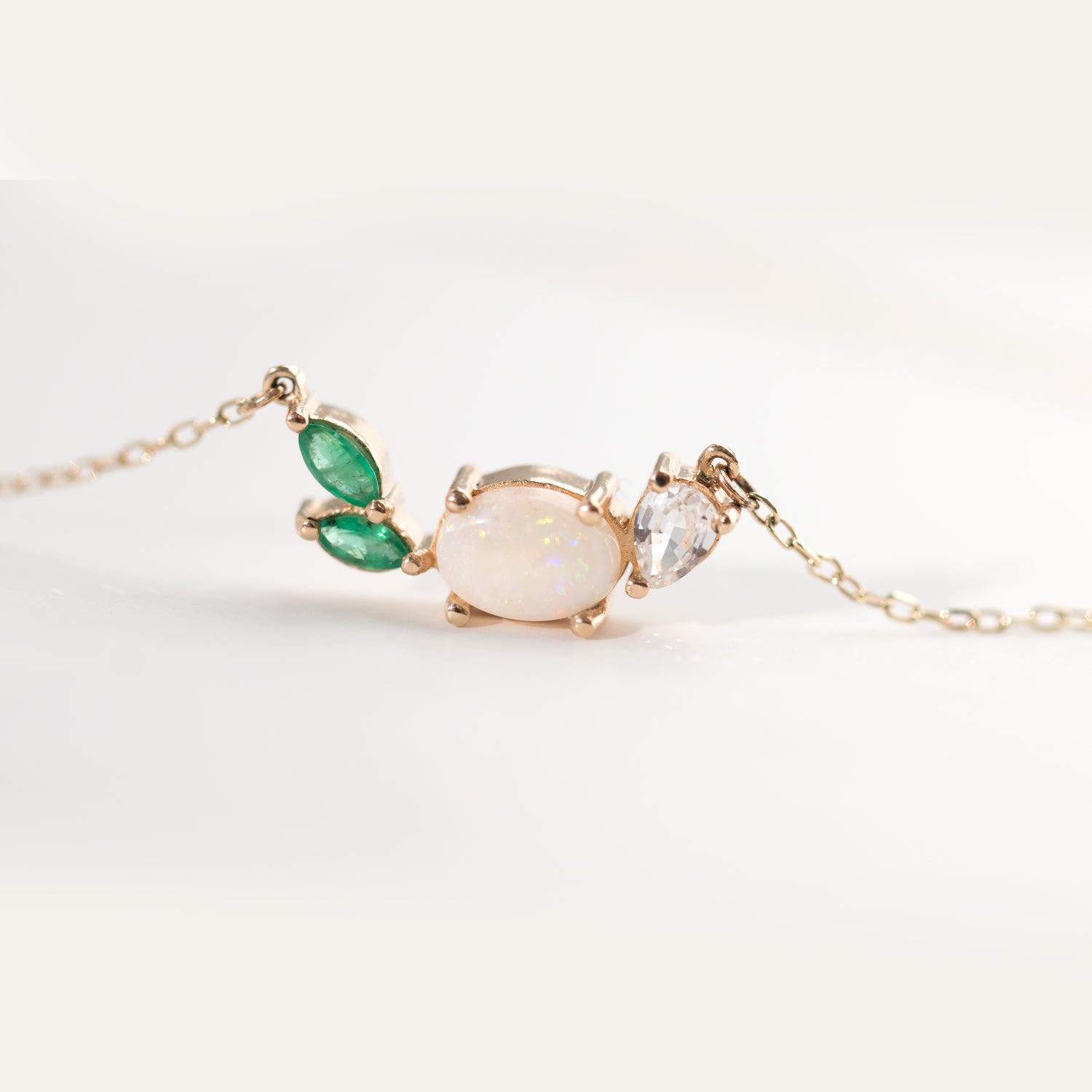 This beautiful, 14K gold-cast necklace is inspired by the tranquility of a lush evergreen. Adorned with a cluster of gorgeous gemstones, including an Australian opal and two emeralds, it's finished with a sparkly pear-cut lab diamond.