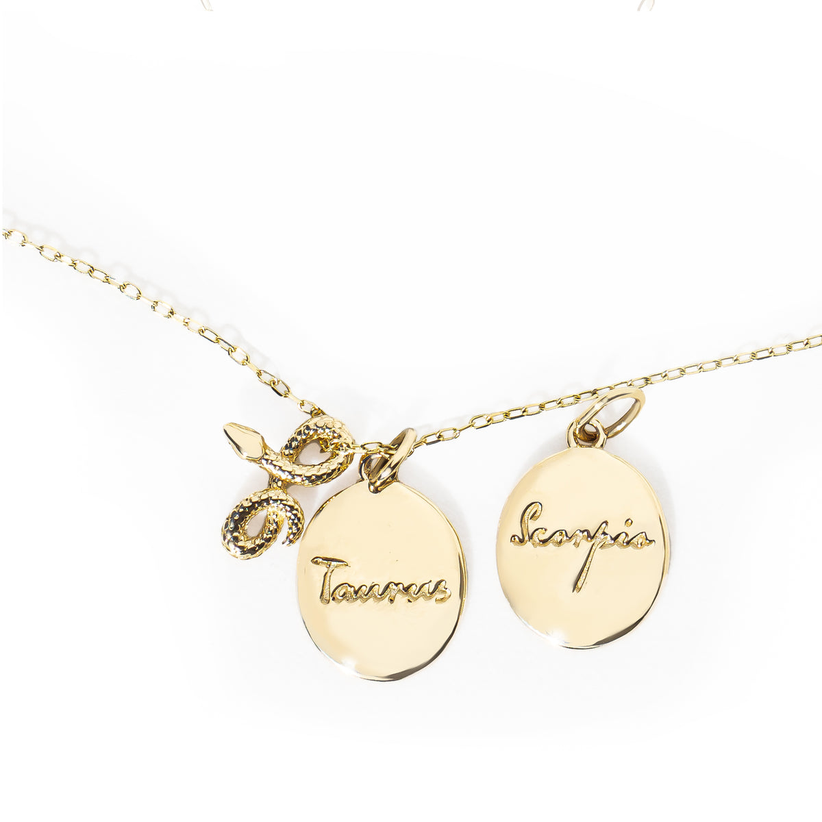 Gold necklace with 'Taurus' and 'Scorpio' pendants and a snake charm on a white background