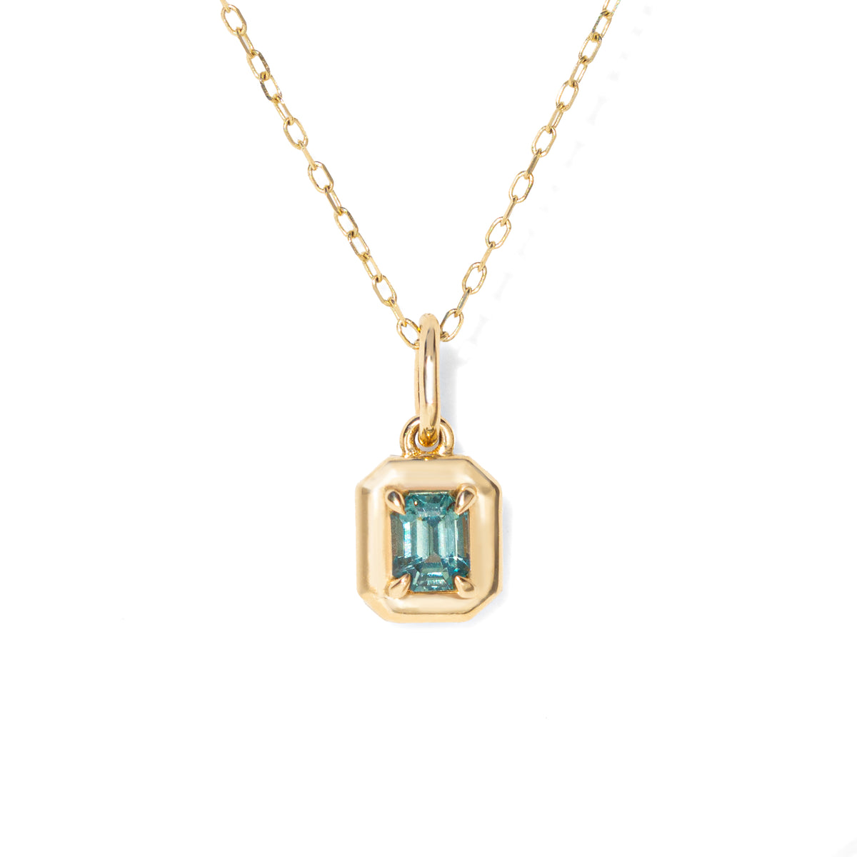 Gold necklace with a pendant featuring a blue green emerald cut sapphire on a white background