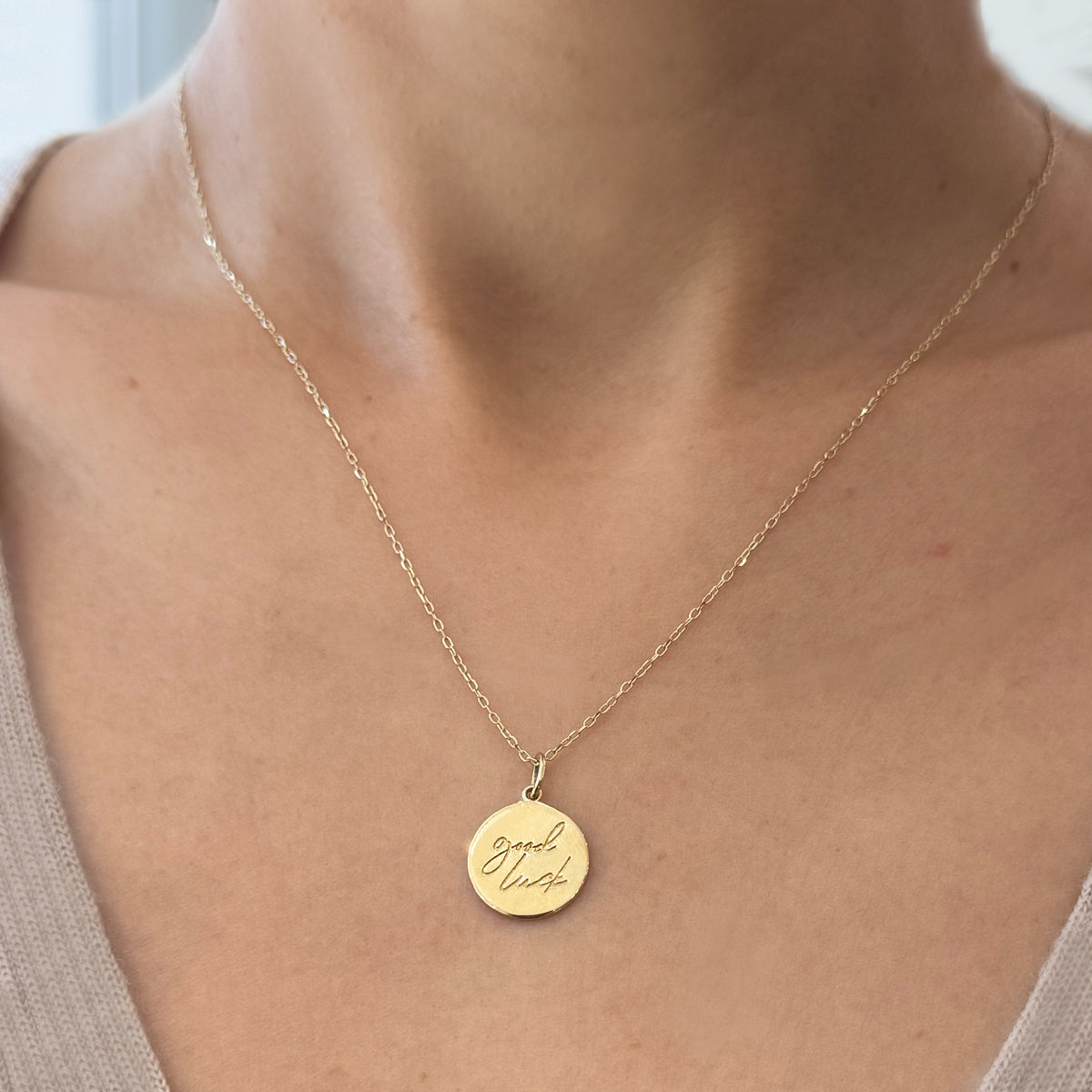 Gold necklace with a round pendant on a person wearing a beige top.