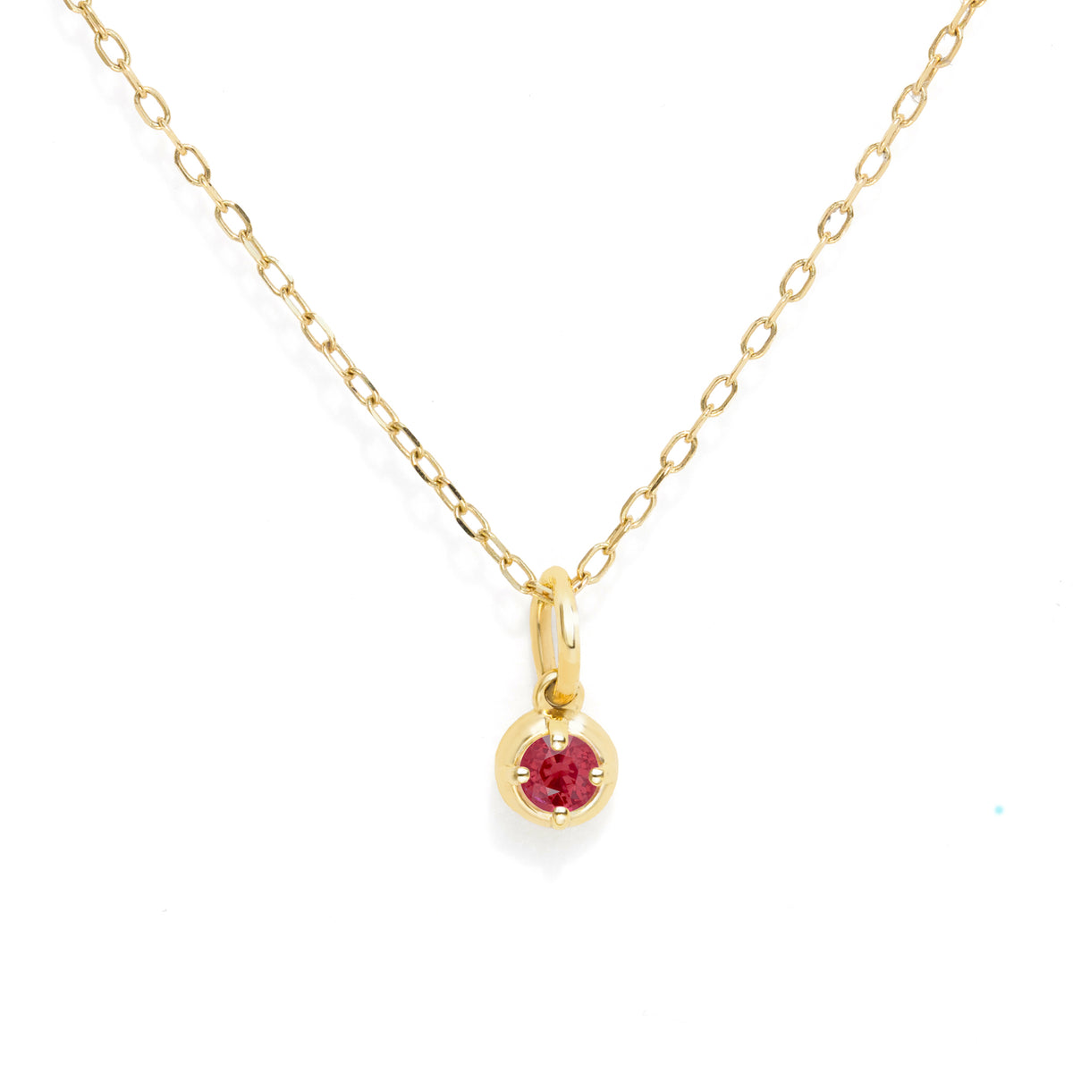 A delicate yellow gold chain necklace with a small round bezel-set red gemstone pendant, shown on a clean white background.