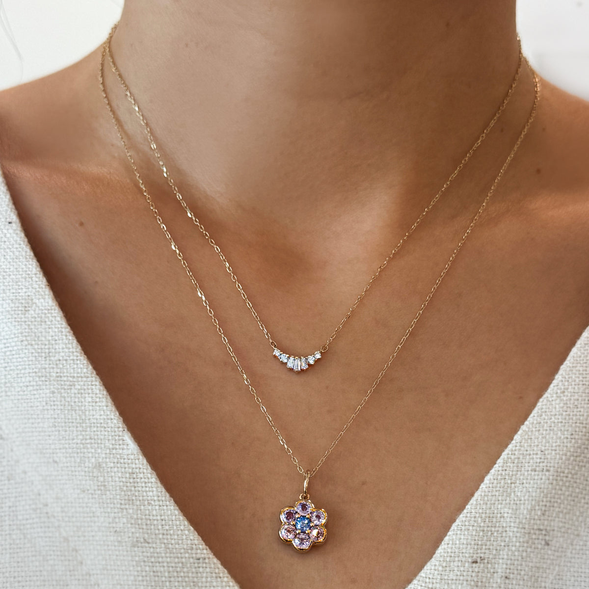 Two gold necklaces with pendants on a person wearing a white top.