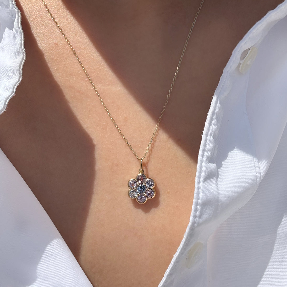 A gold flower-shaped pendant necklace with clear stones, worn on a model's neck over a white collared shirt.