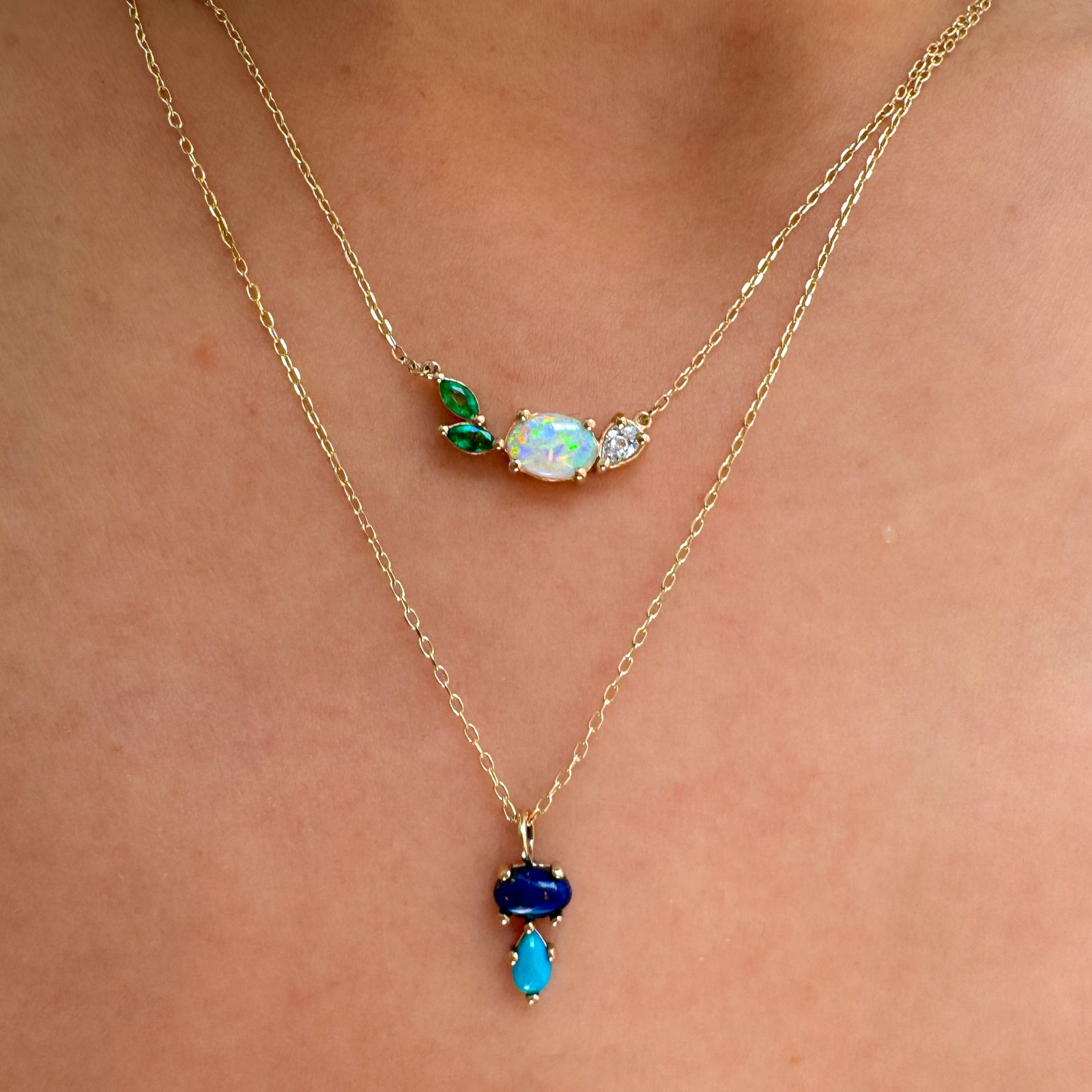 Two gold necklaces with opal pendants on a person's neck.