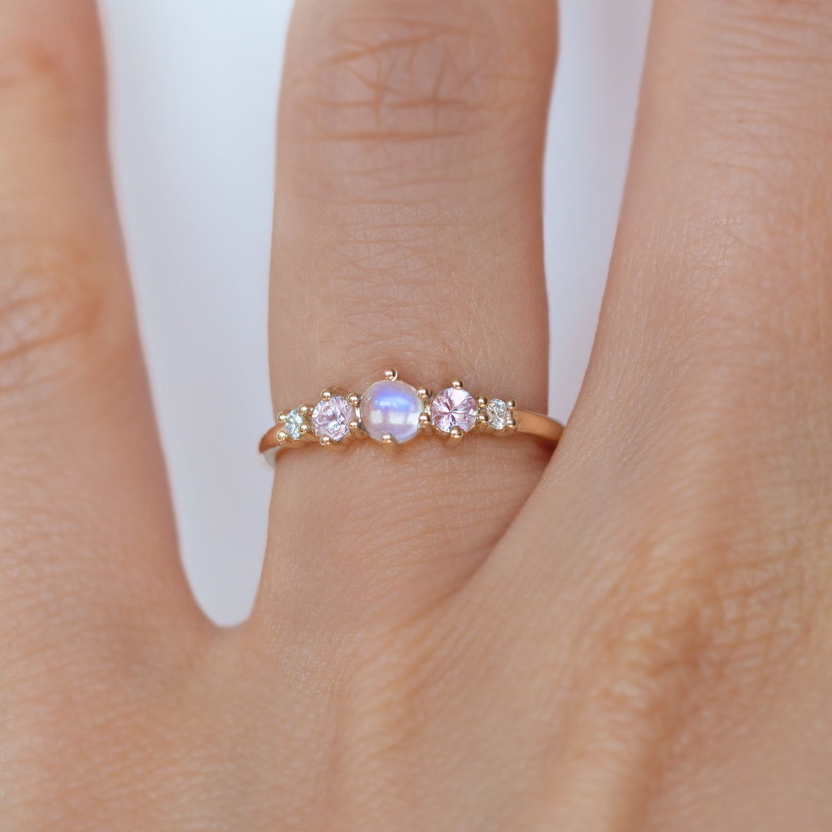 The classic Georgia design makes this five stone ring ideal for everyday wear. This unique ring features a round rainbow moonstone, adorned with natural pink sapphires and diamonds, and exudes mystical purple blue hues, making it a true unicorn piece.