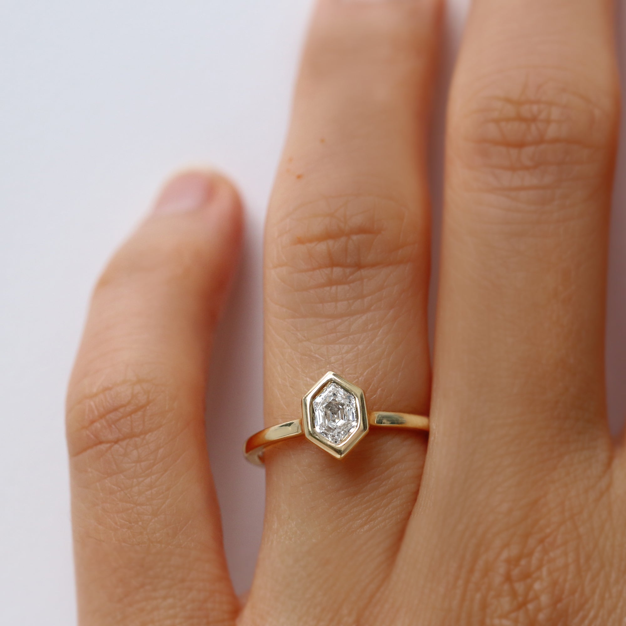 Gold ring with a hexagon diamond on a person's finger against a white background