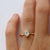 Gold ring with a hexagon diamond on a person's finger against a white background