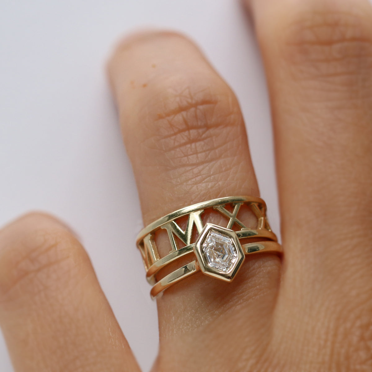 Gold ring with a hexagon diamond on a finger against a white background