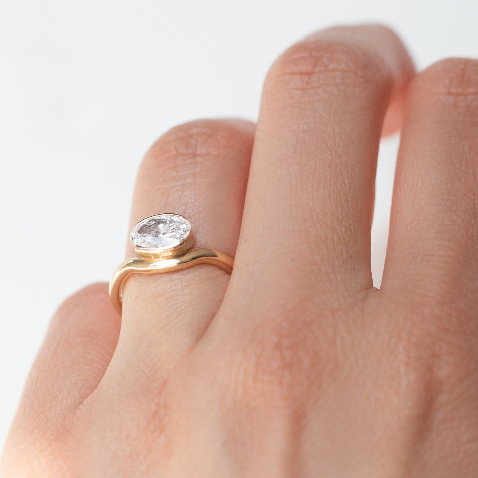 The Flow Ring features a 1 carat oval diamond or moissanite in a half bezel setting. The east west design adds a unique touch to this minimalistic design, making it the perfect subtle statement ring.