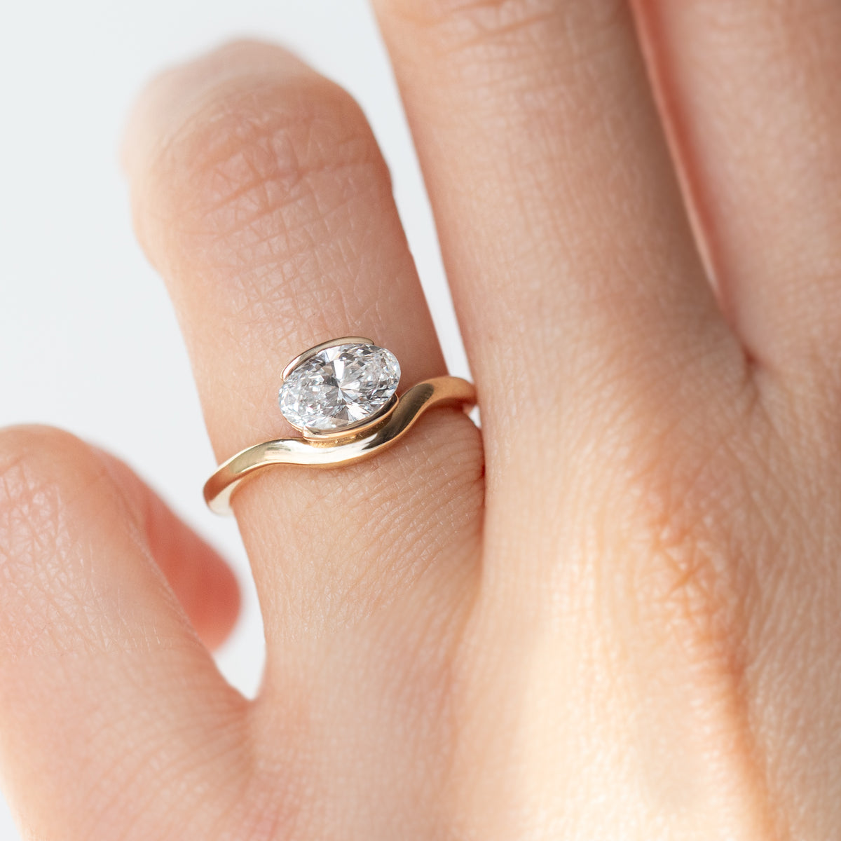 The Flow Ring features a 1 carat oval diamond or moissanite in a half bezel setting. The east west design adds a unique touch to this minimalistic design, making it the perfect subtle statement ring.