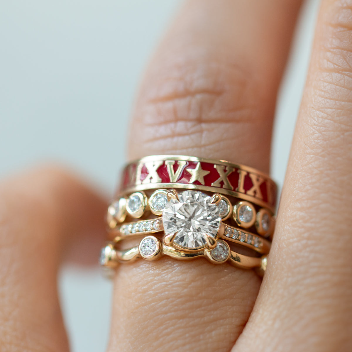 Gold ring with diamond and Roman numeral design on a finger against a neutral background