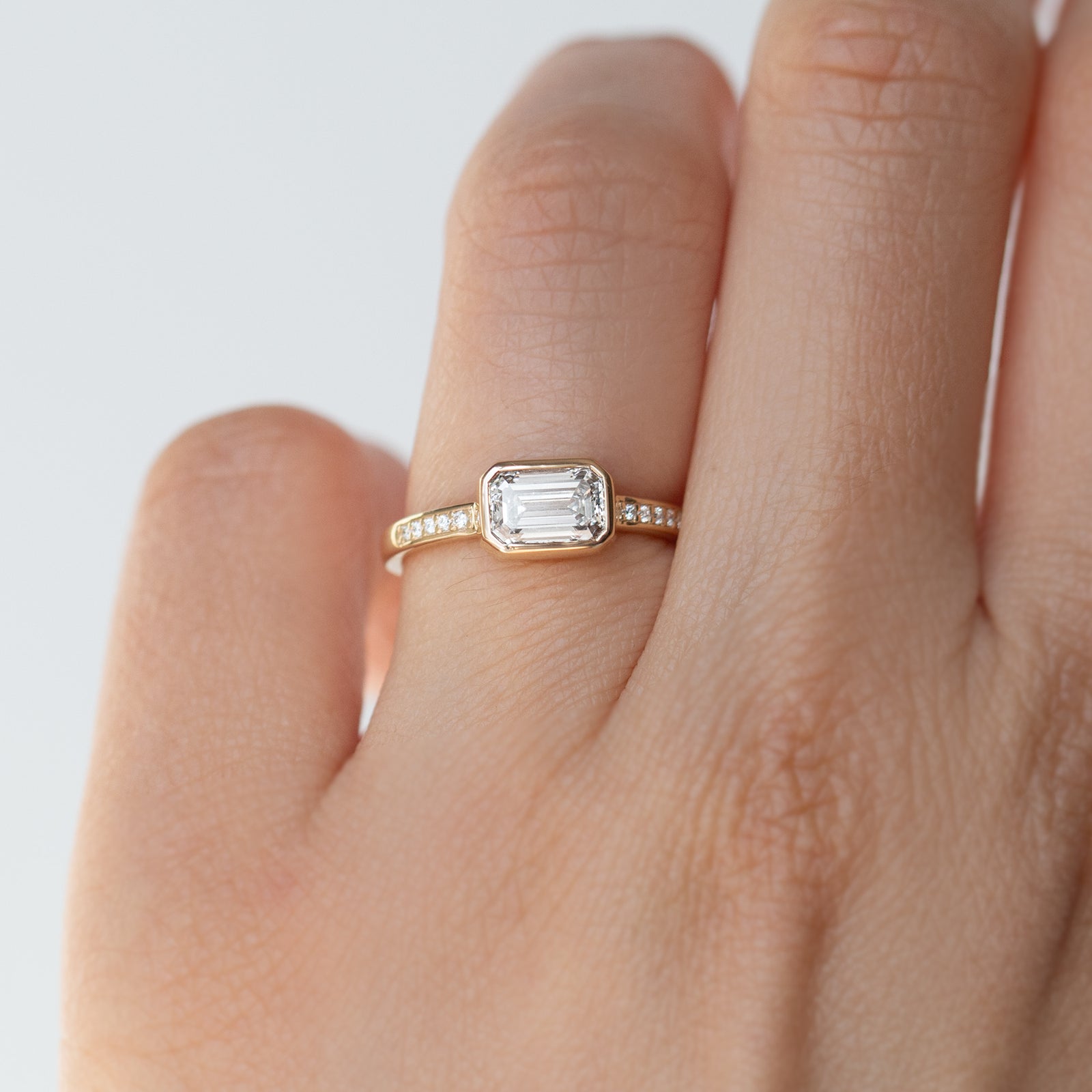 The Zoey Ring features a 1-carat emerald-cut diamond or moissanite in an east-west setting. The smooth bezel setting ensures everyday wear, while delicate accent diamonds add sparkle from every angle