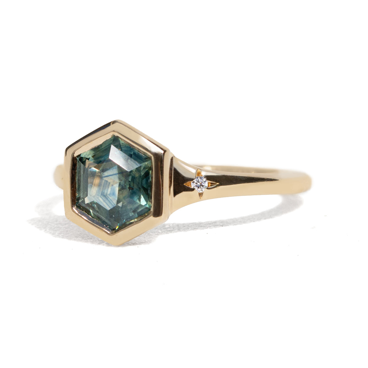 Gold ring with a green hexagon sapphire with two side diamonds on a white background