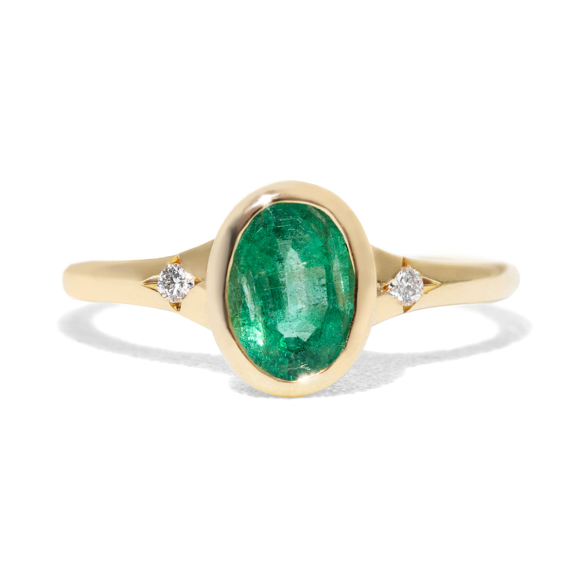  an oval emerald set gold ring and a contour gold band accented with thre diamonds on white background. 