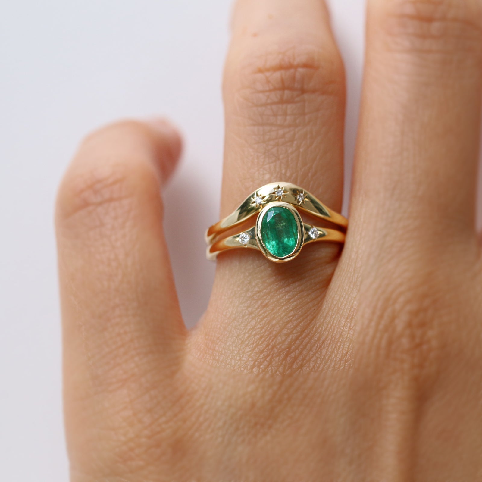 Gold ring with a green gemstone on a finger against a white background