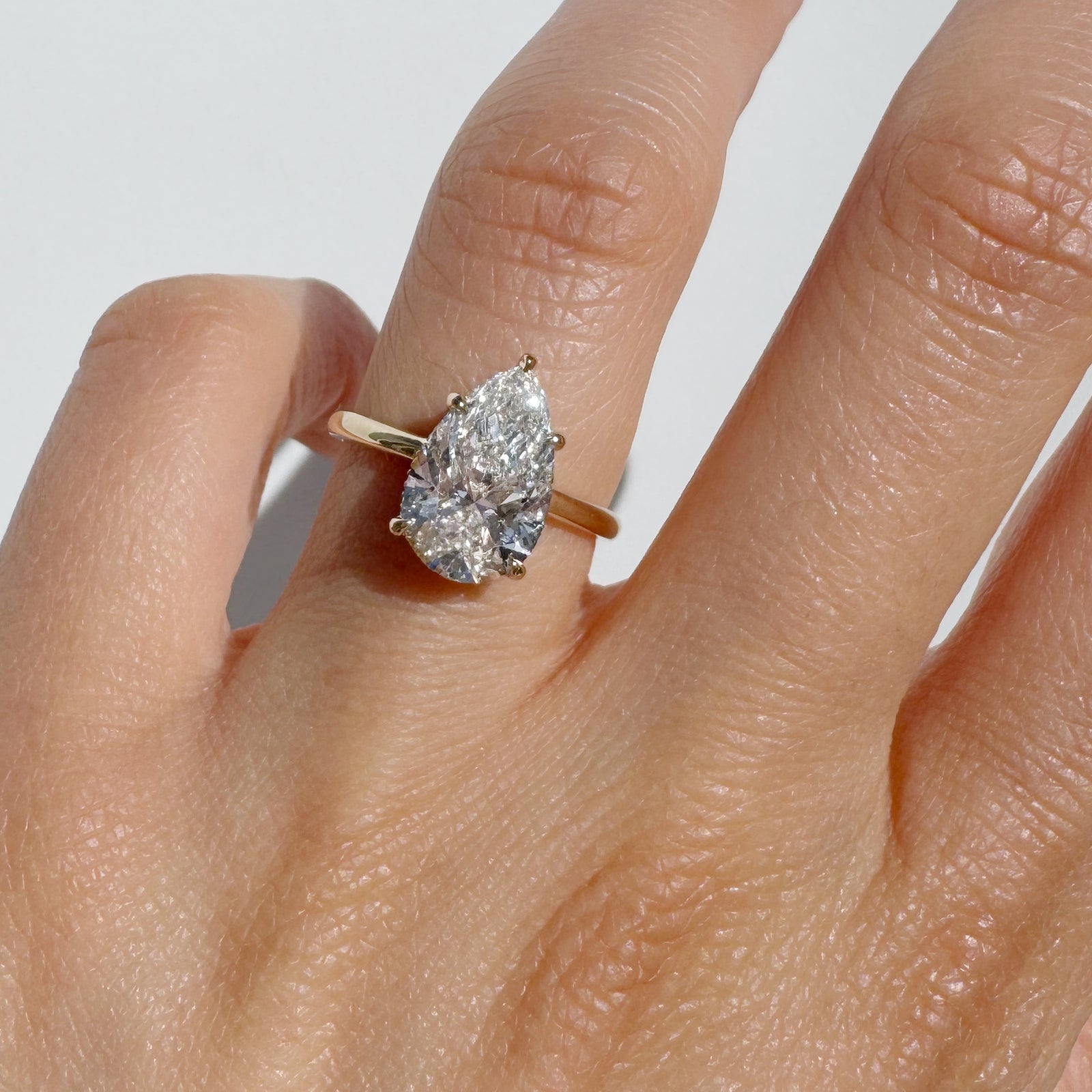 A pear cut diamond ring on a hand against white background.