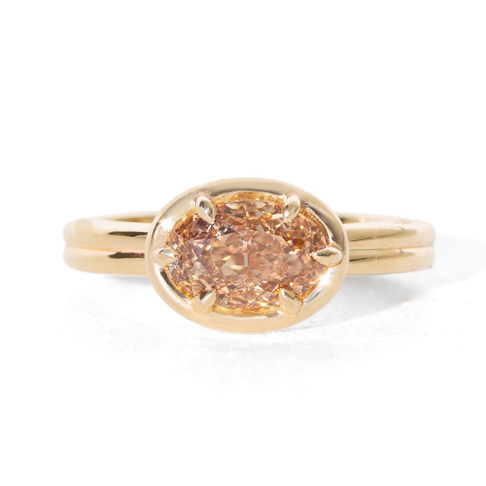 A yellow gold oval ring featuring a light brown-colored oval diamond in a six-prong setting, shown on a clean white background.