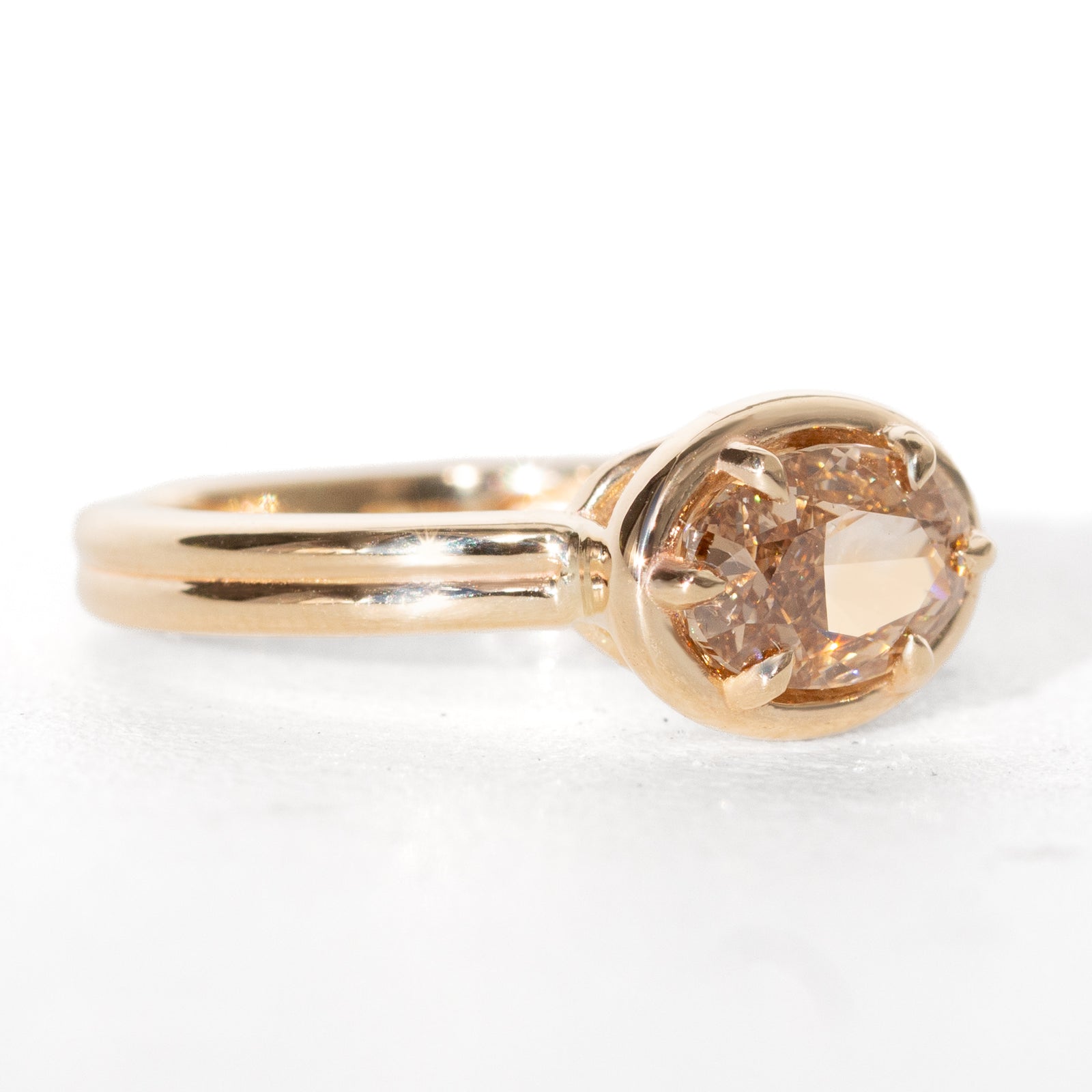 A yellow gold oval ring featuring a light brown-colored oval diamond in a six-prong setting, shown on a clean white background.