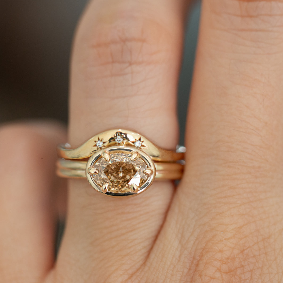 A close-up of a gold ring with a round diamond center stone and small star details on the band, worn on a finger.