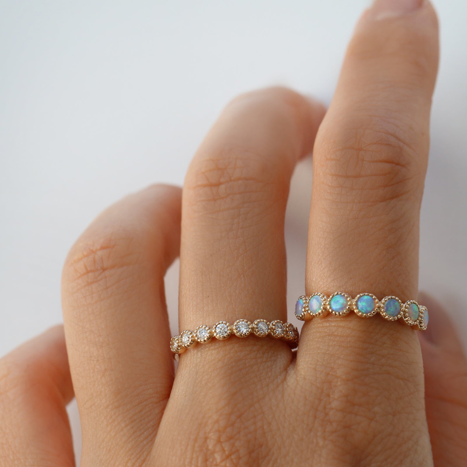 Hand wearing two rings with opal and diamond gemstones  on a light background