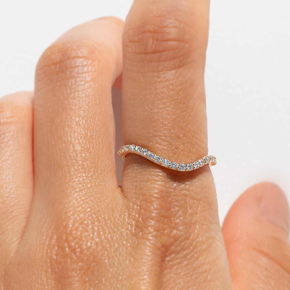 gold ring with small diamonds on a finger against a light background