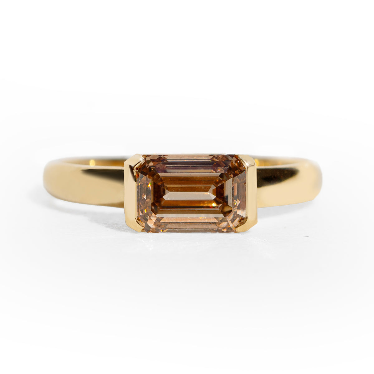 Gold ring with an emerald cut champagne diamond  on a white background