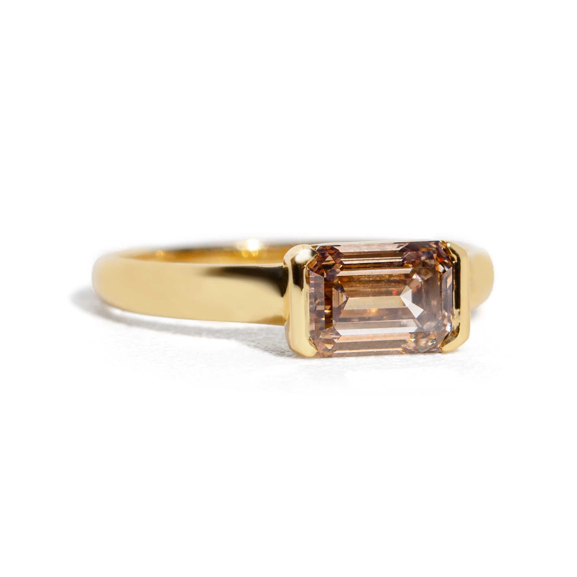 Gold ring with an emerald cut champagne diamond  on a white background