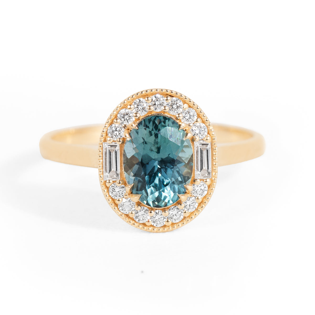 Gold ring with a teal sapphire gemstone and diamond accents halo on a white background