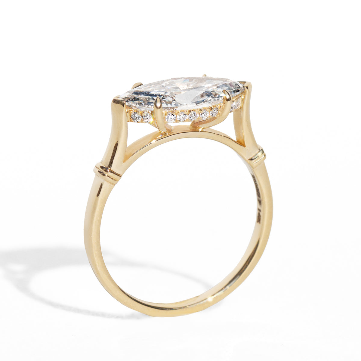 Gold ring with a large marquise diamond and smaller diamonds on the hidden halo against a white background