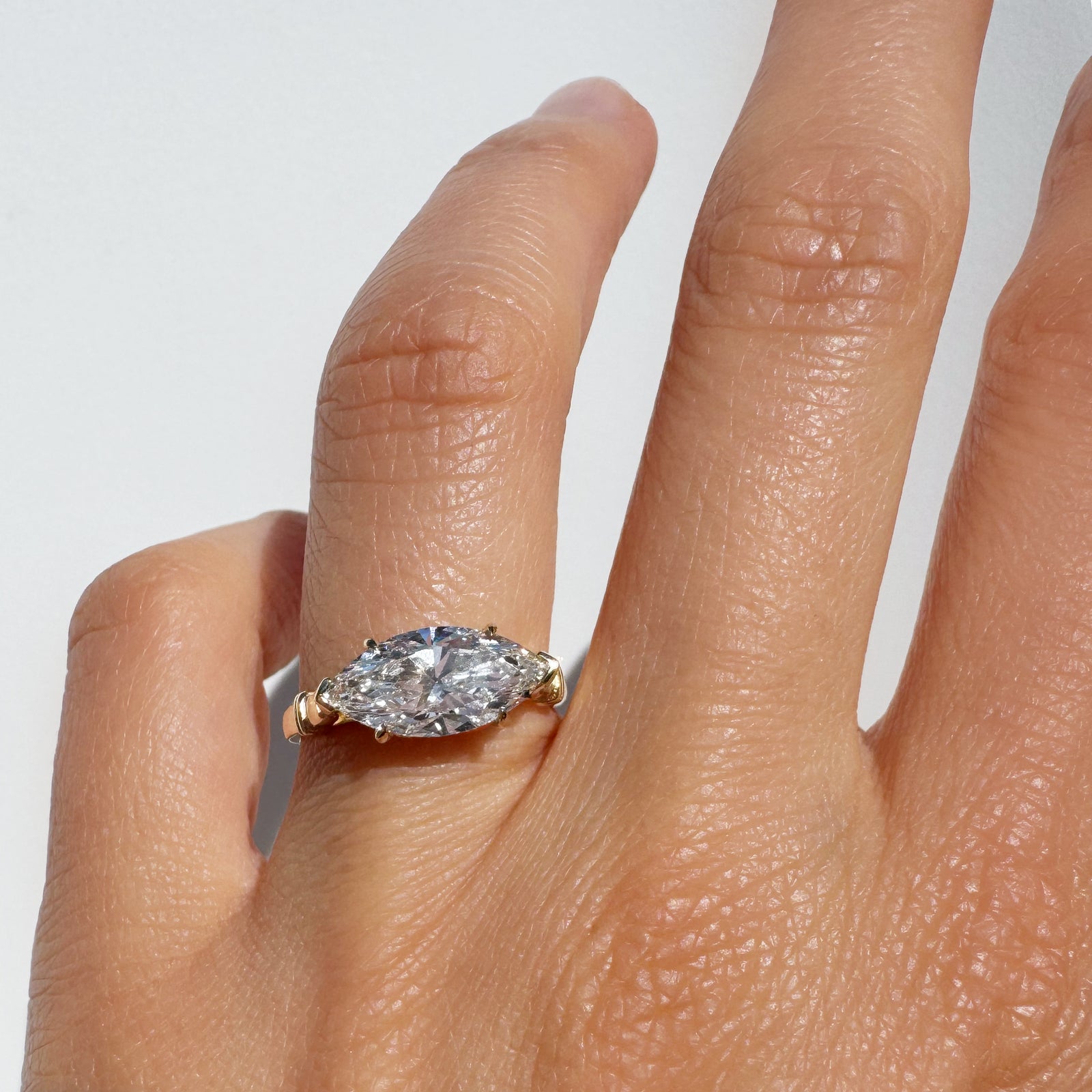 Gold ring with a diamond on a person's finger against a white background