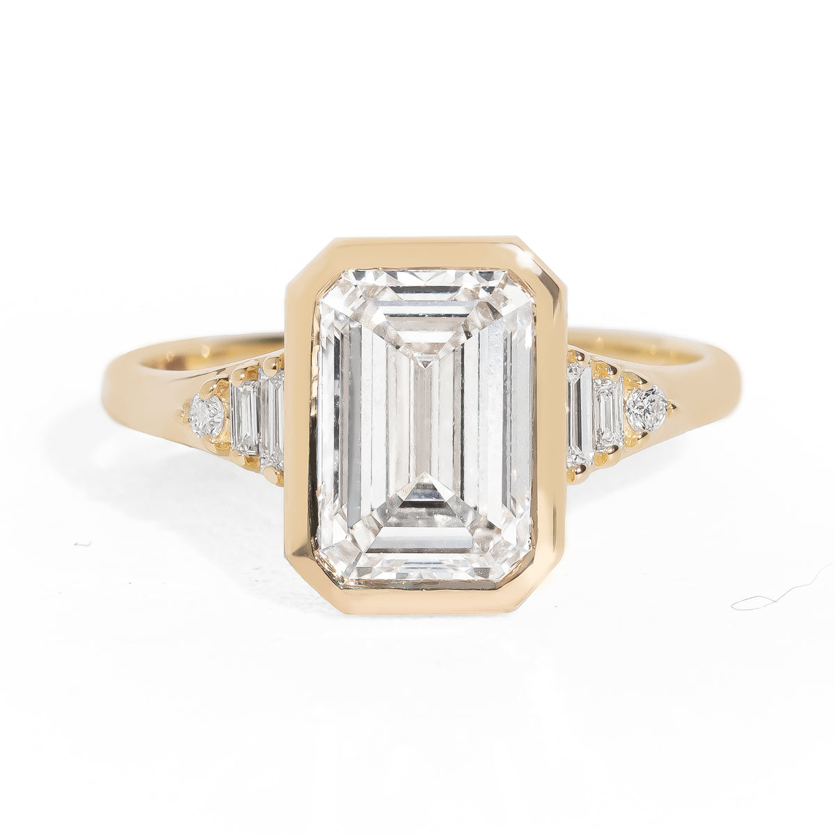 Gold ring with emerald-cut diamond and baguette diamonds on a white background