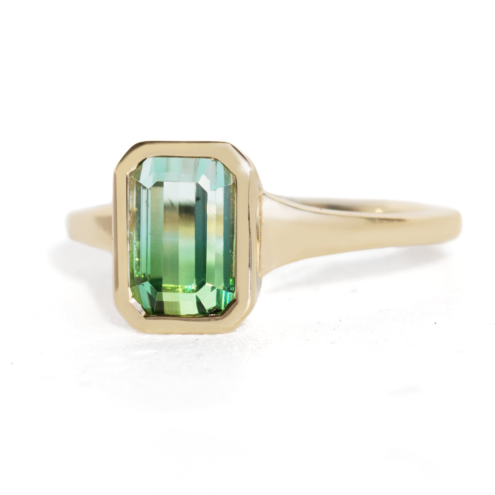 A yellow gold ring featuring a rectangular emerald-cut green gemstone, set against a clean white background.