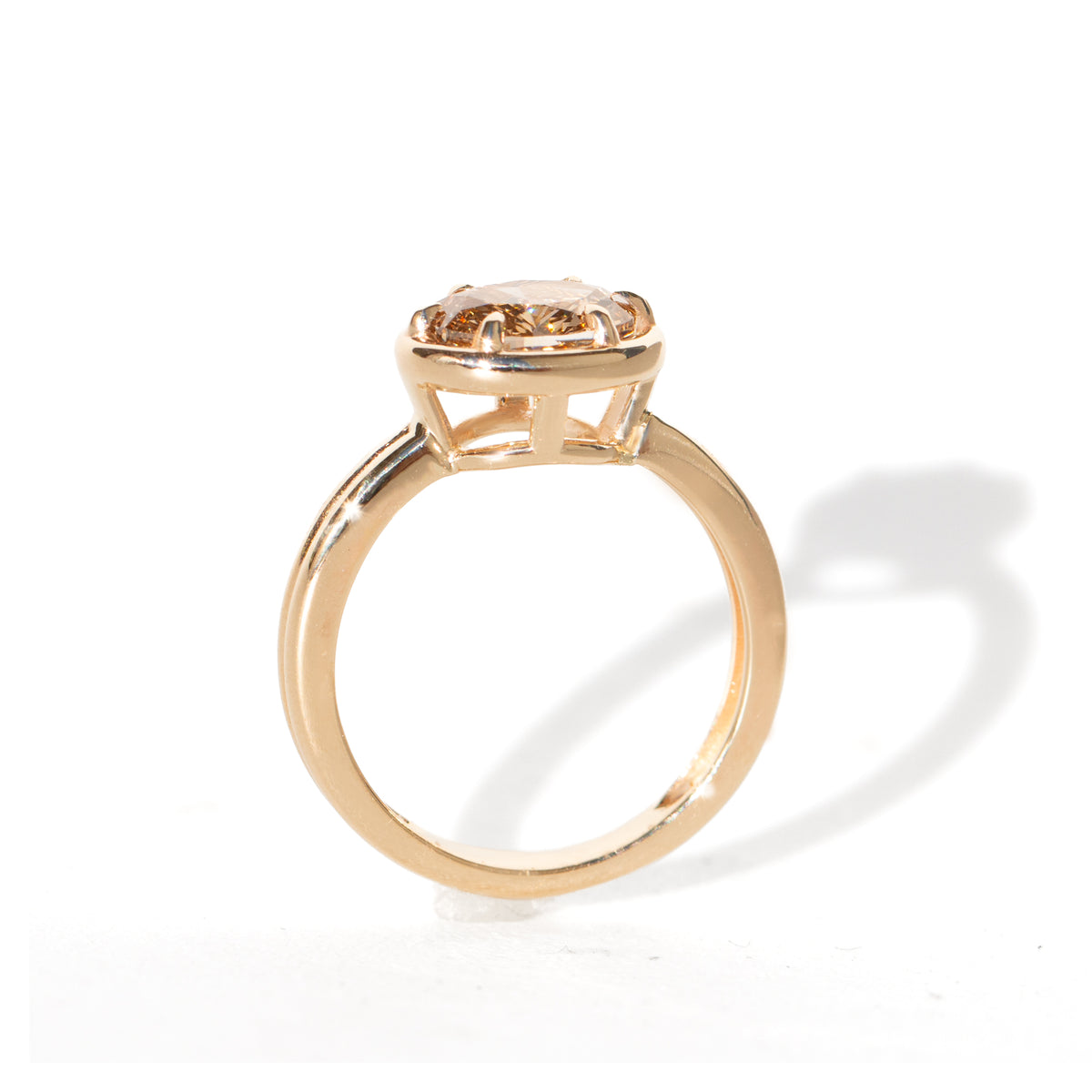 A yellow gold oval ring featuring a light brown-colored oval diamond in a six-prong setting, shown on a clean white background.