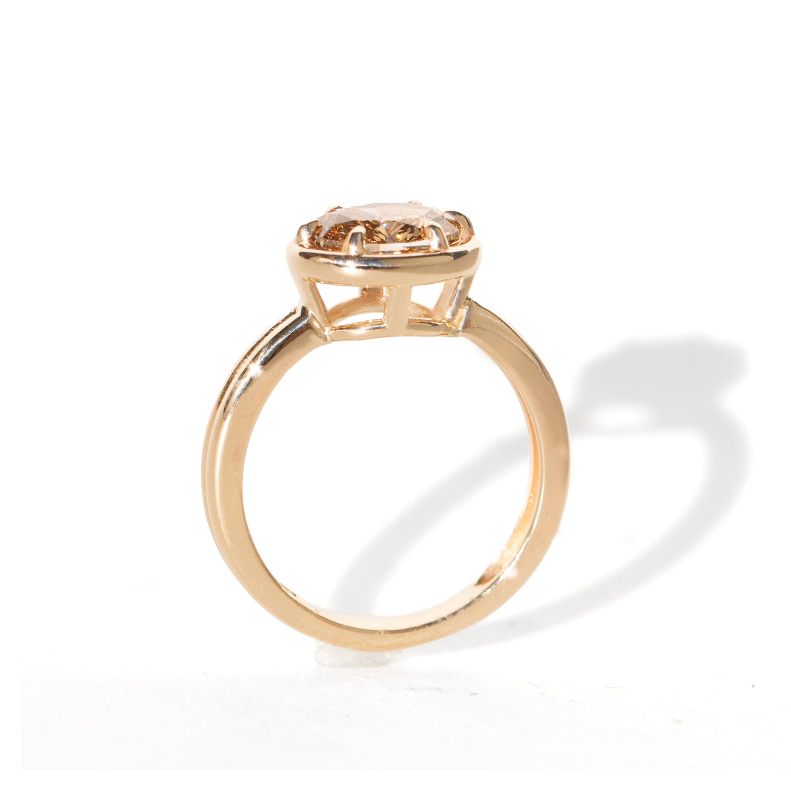 A yellow gold oval ring featuring a light brown-colored oval diamond in a six-prong setting, shown on a clean white background.