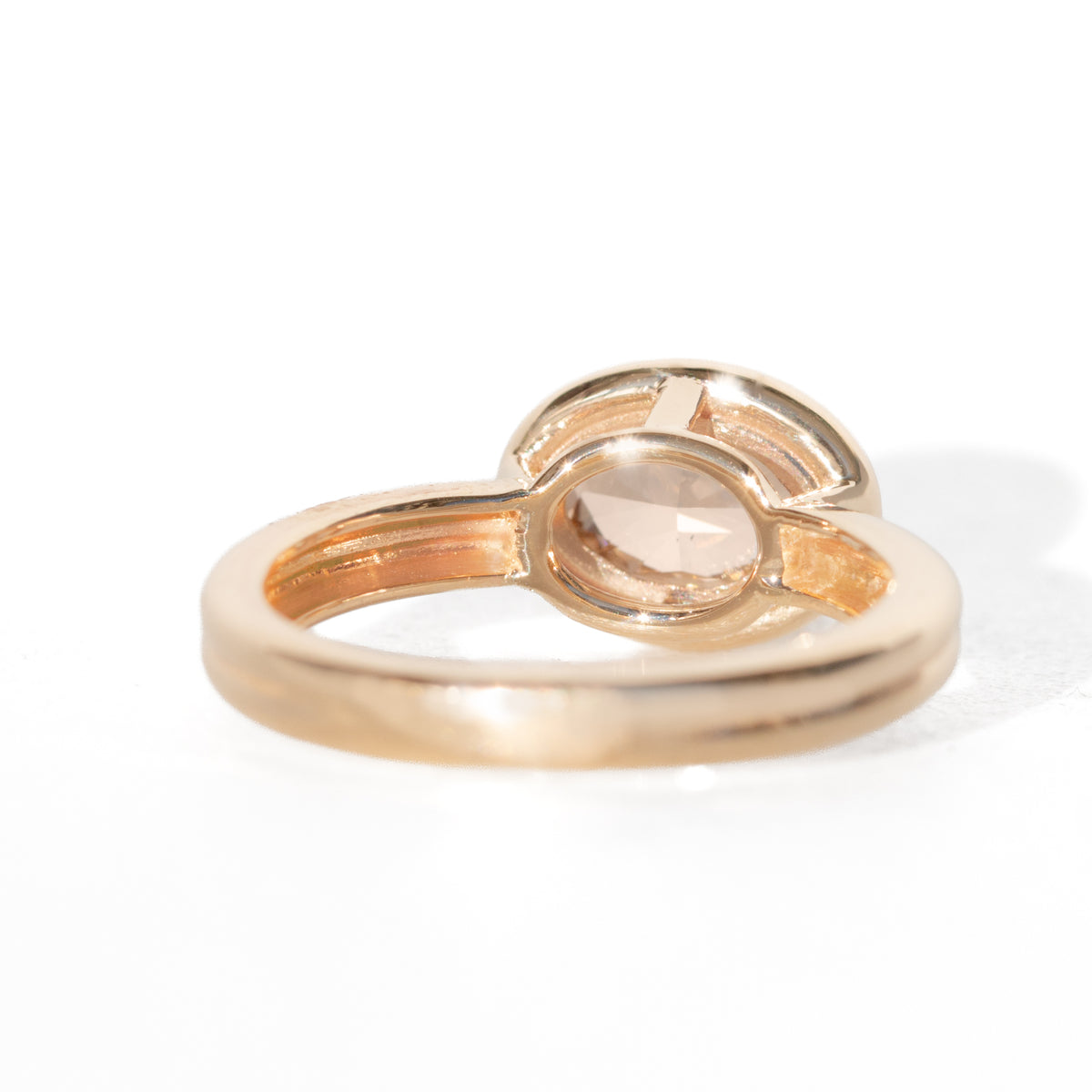 A yellow gold oval ring featuring a light brown-colored oval diamond shown on a clean white background. Showing the bottom of the ring. 