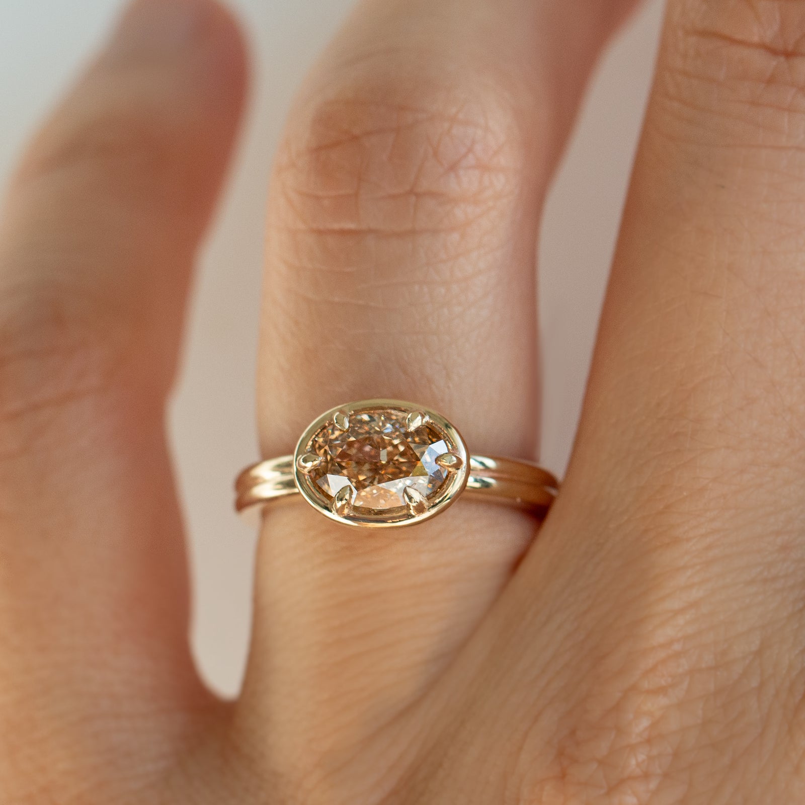 A yellow gold oval ring featuring a light brown-colored oval diamond in a six-prong setting on a finger.