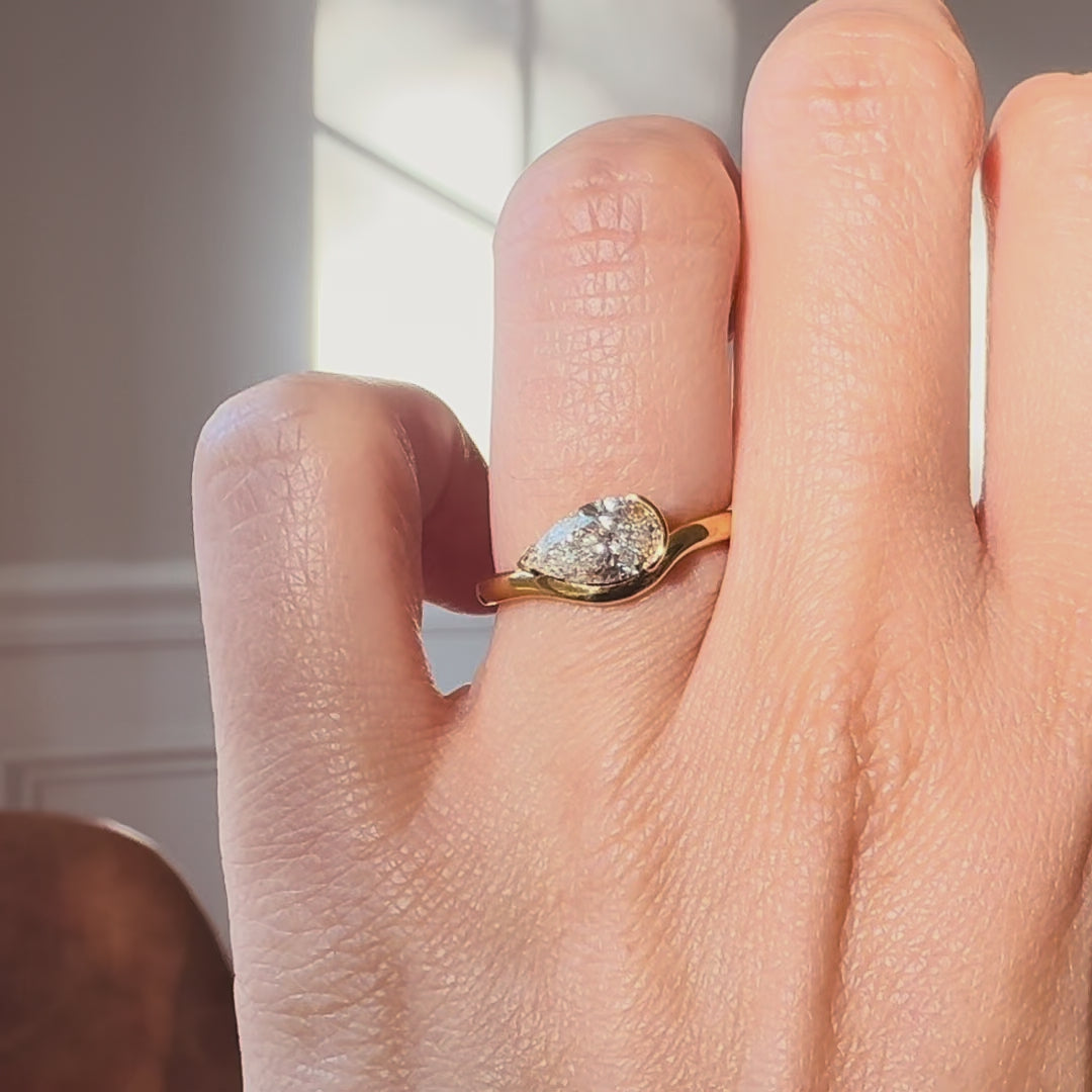 Pear cut diamond ring on a hand against a neutral background. 