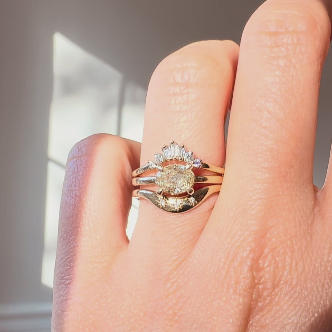 a champagne color diamond engagement ring and two diamond bands on a hand against a neutral background. 