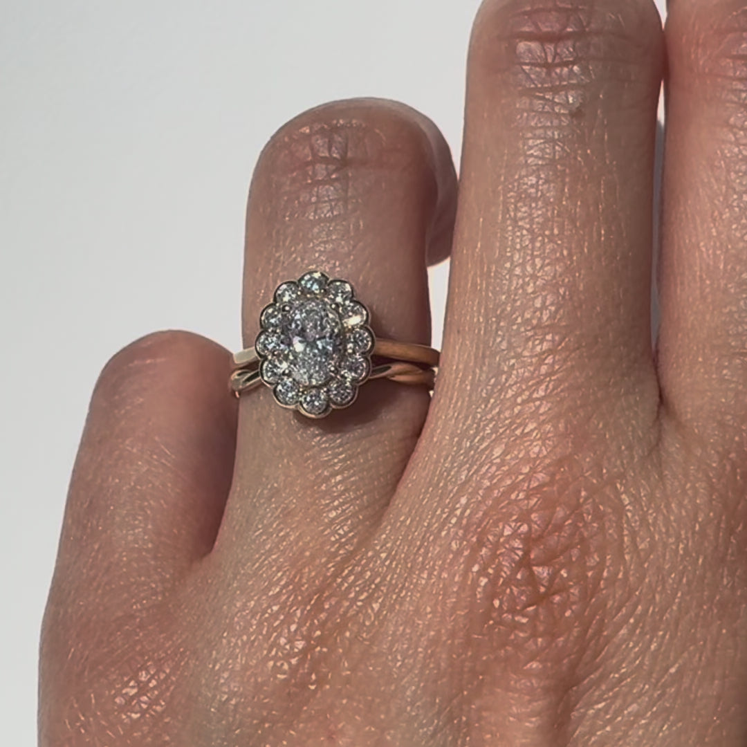 Gold ring with an oval diamond with a halo on a hand against a white background